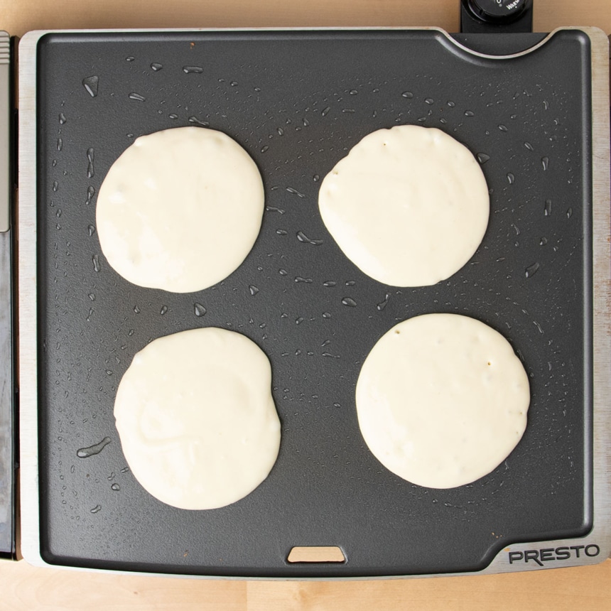 4 raw round pancakes cooking on hot greased black griddle