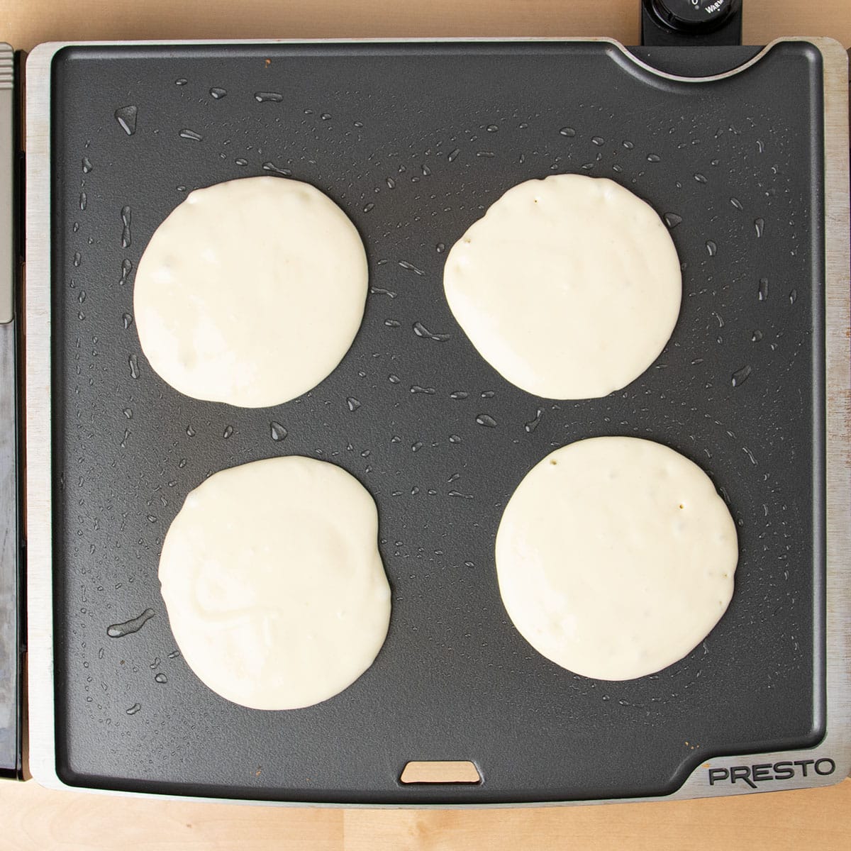 Four raw round pancakes cooking on hot griddle.