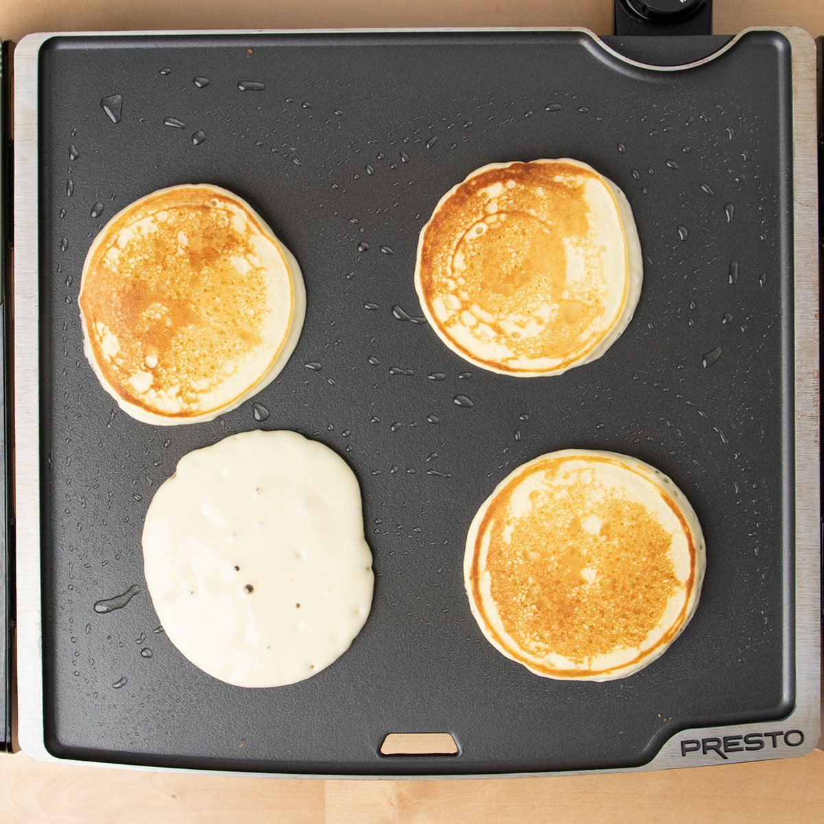 Three pancakes cooked and one uncooked on black griddle.