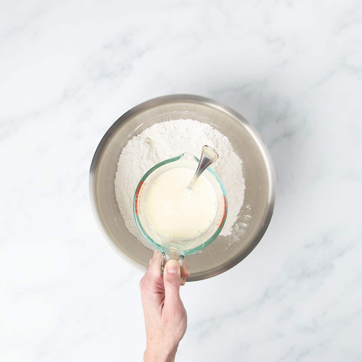 Hand holding glass measuring bowl with fork having whisked egg and milk.