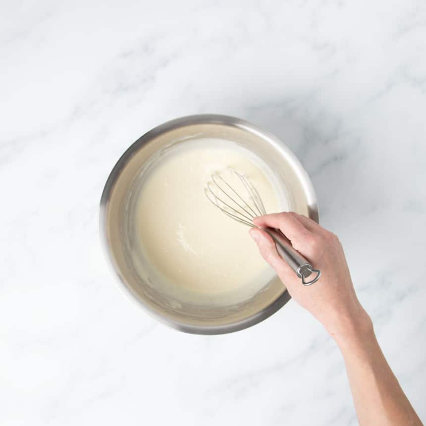 hand holding wire whisk in pancake batter in same mixing bowl