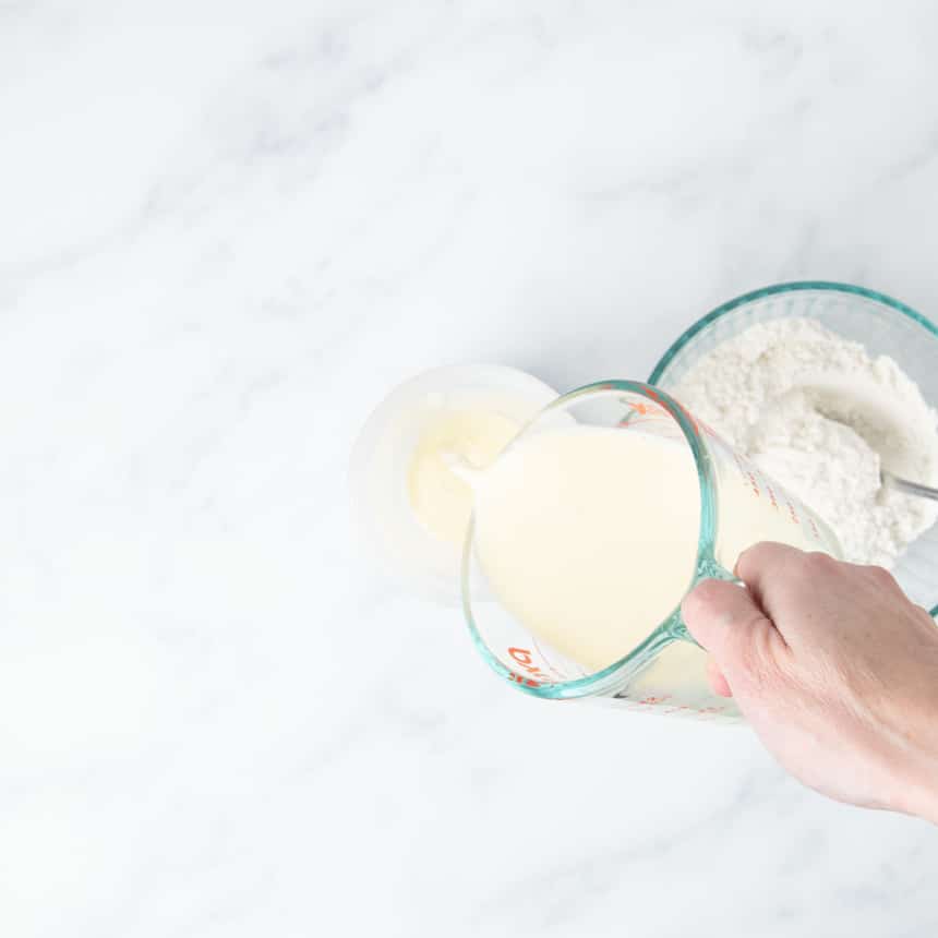 hand pouring egg and milk mixture into plastic pancake blender bottle