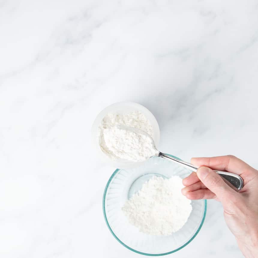 hand holding spoon putting dry ingredients into blender bottle