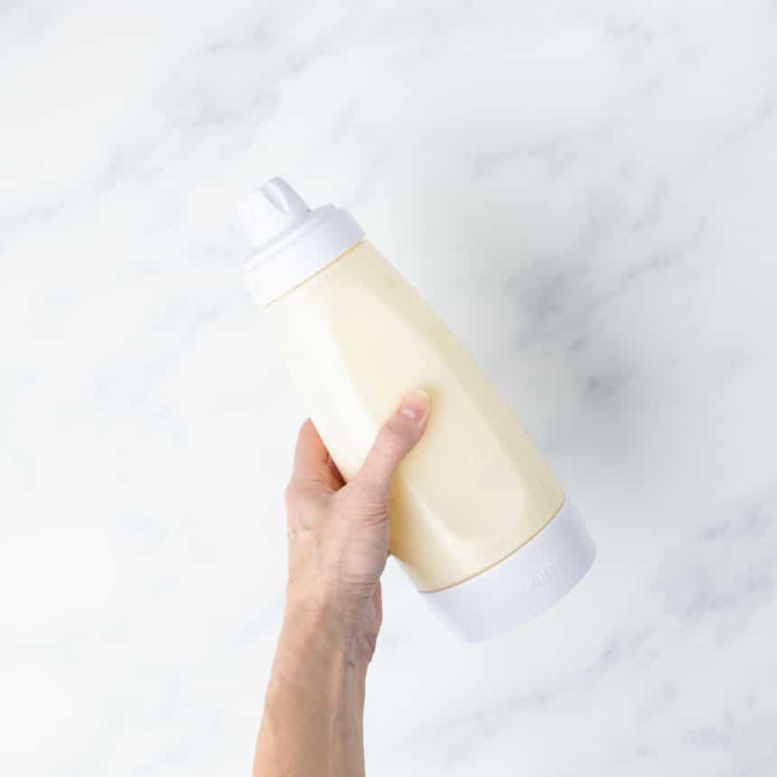 hand holding shaken plastic pancake blender bottle with raw pancake mixture and white top and bottom secured