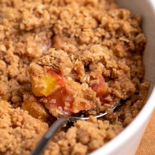 gluten free peach crisp with serving spoon in white casserole dish