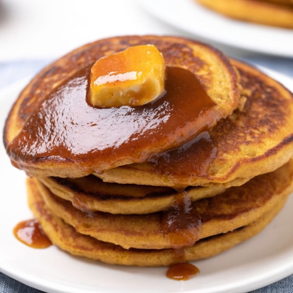 stack of 6 gluten free pumpkin pancakes with syrup and butter on white plate