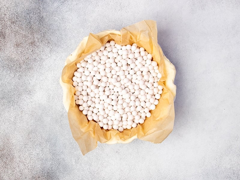 brown paper lining shaped raw pie crust filled with white round pie weights