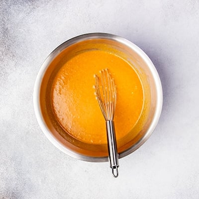 same metal whisk sitting in orange liquid in same metal mixing bowl