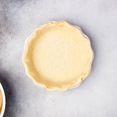 parbaked light tan pie crust with fork piercings in white pie dish