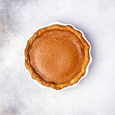 whole baked brown pie crust with dark orange and brown colored baked filling in same white pie plate