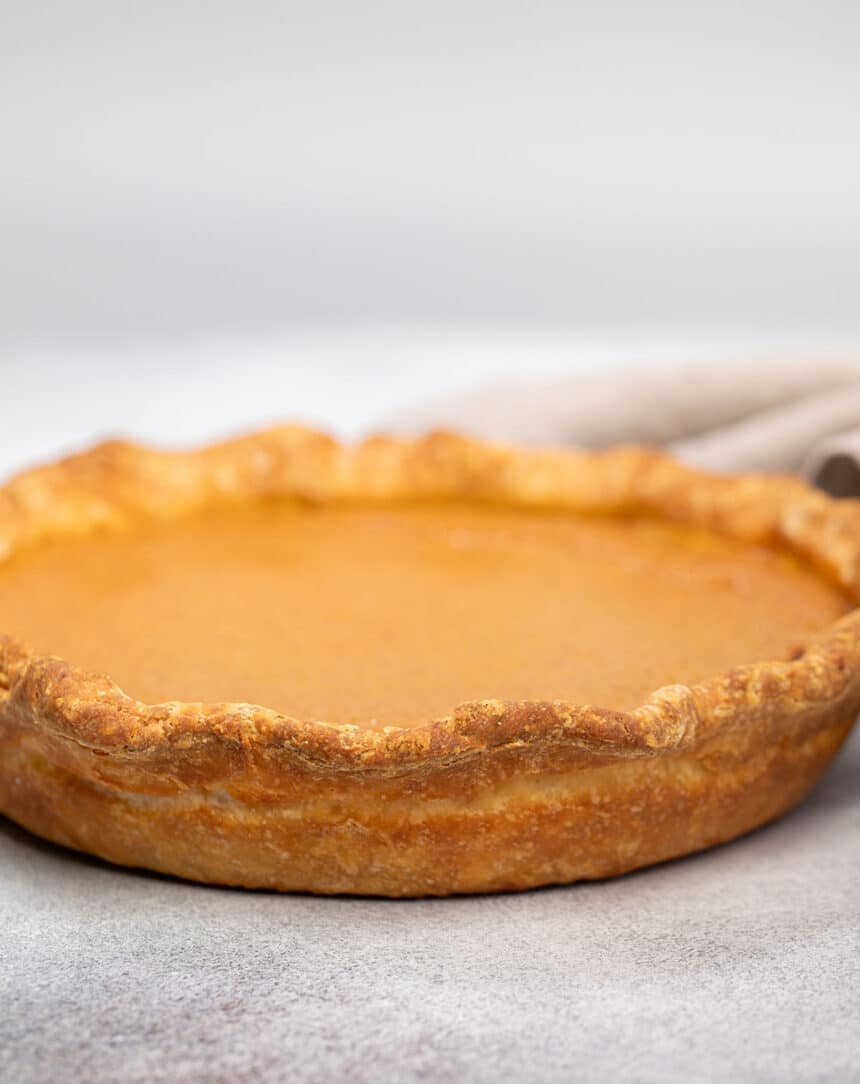 whole uncut pie with orange filling and browned crust out of pie dish on gray surface