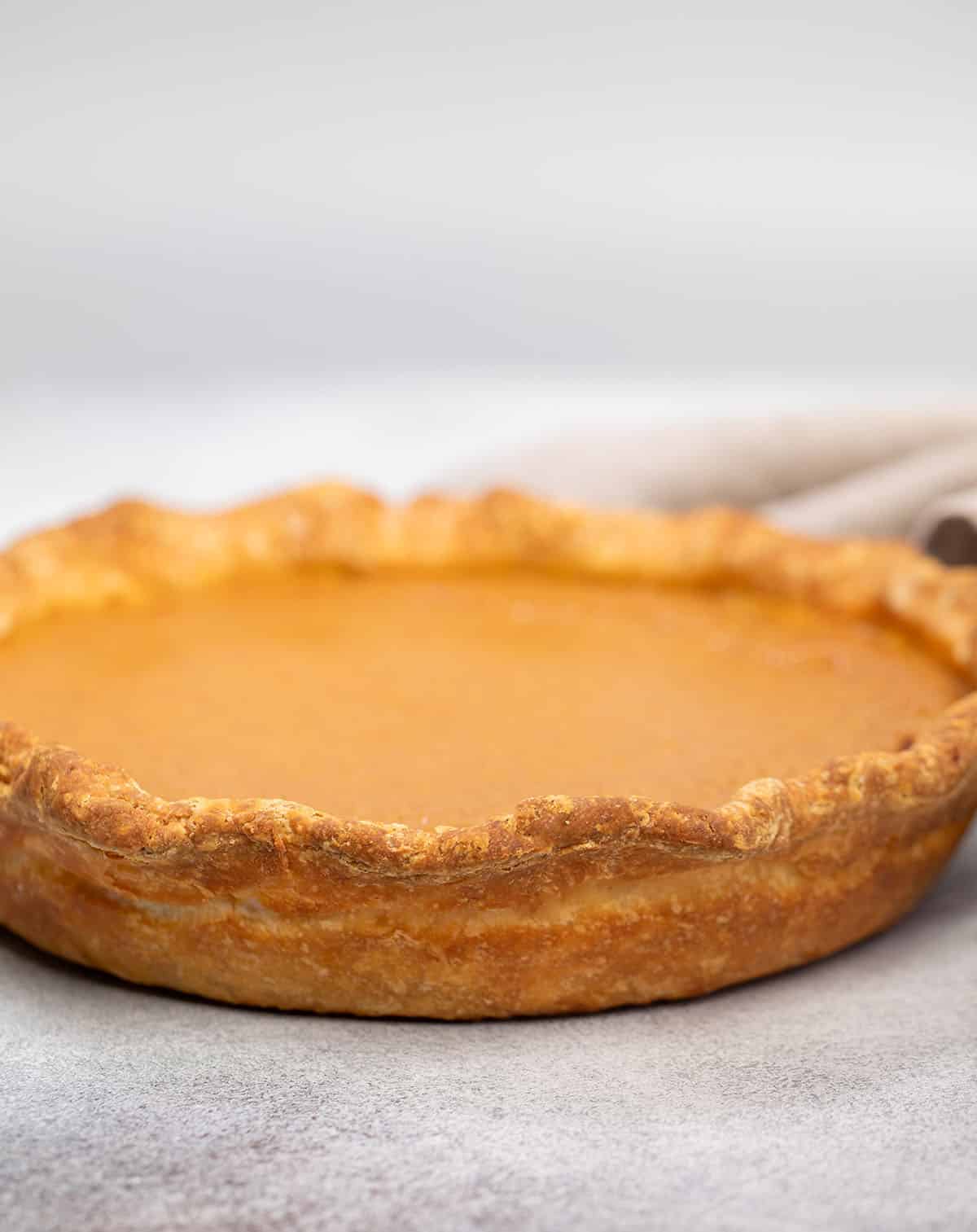 Whole uncut pie with orange filling and browned crust out of pie dish on gray surface.