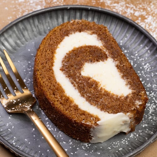 slice of gluten free pumpkin roll with white swirl filling on gray plate with gold fork