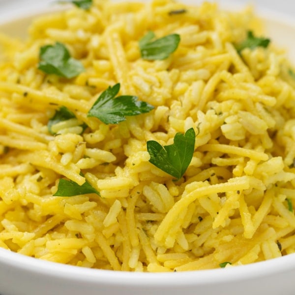 yellow colored gluten free rice a roni in white bowl with parsley leaves