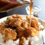 sauce pouring on gluten free sesame chicken on rice in white bowl