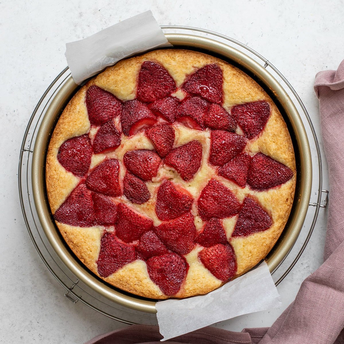 overhead image of gluten free strawberry cake in round metal baking pan on wire rack