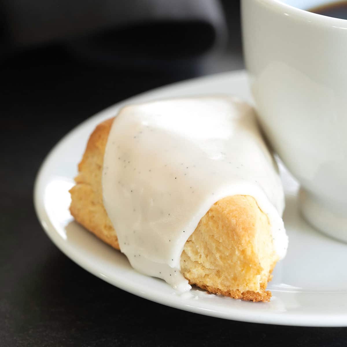 gluten free vanilla scone on small white plate with cup of coffee