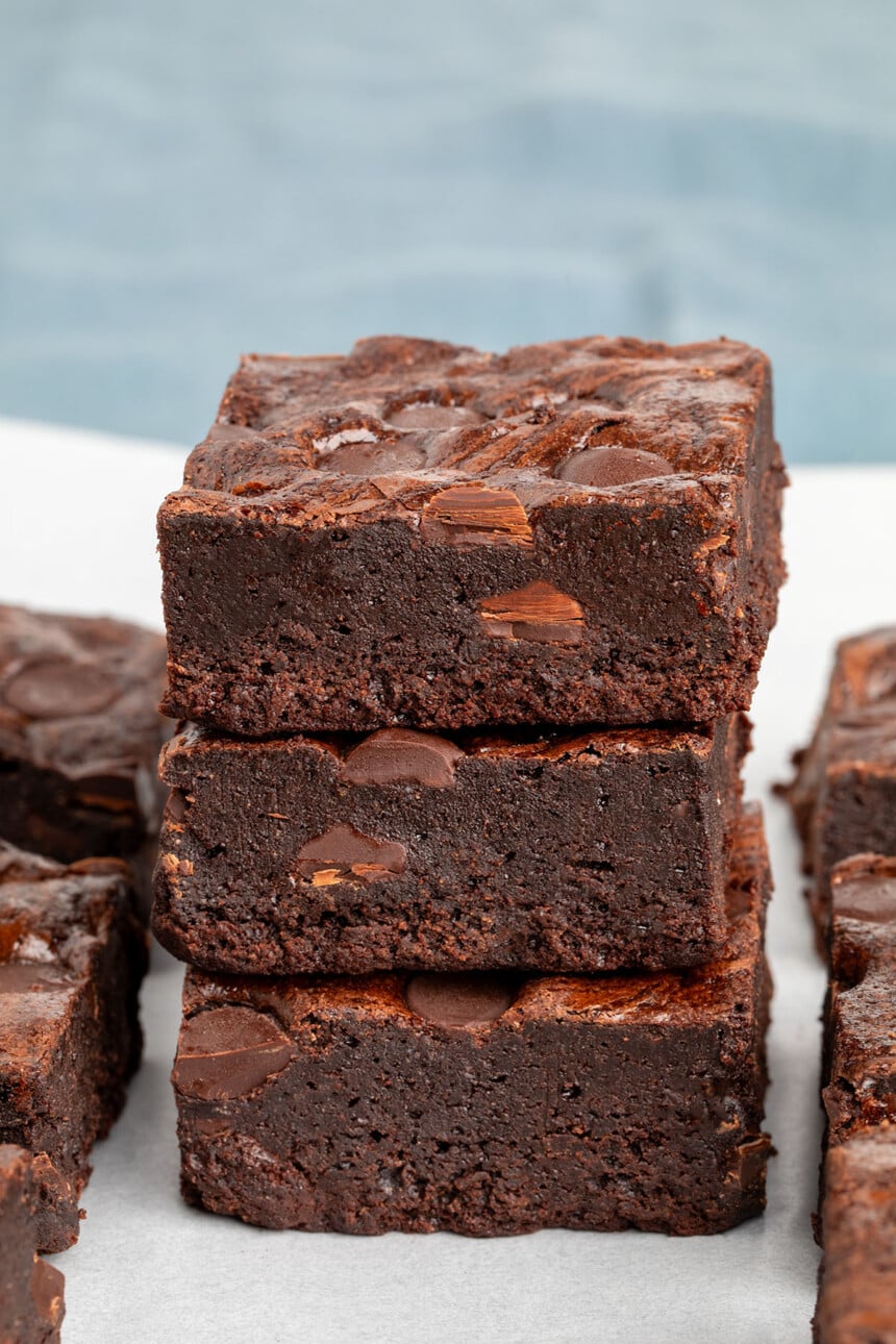 vertical stack of 3 oat flour brownies with chocolate chips on white paper with blue cloth in background