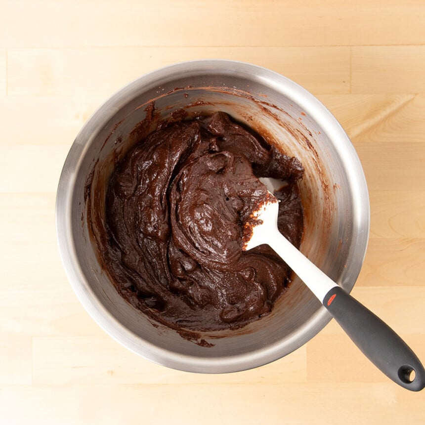 dark brown brownie batter with chocolate chips in metal mixing bowl with white spatula