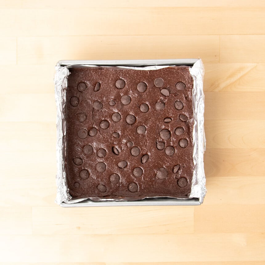 overhead image of unbaked metal square baking pan of dark brown batter with chocolate chips on top