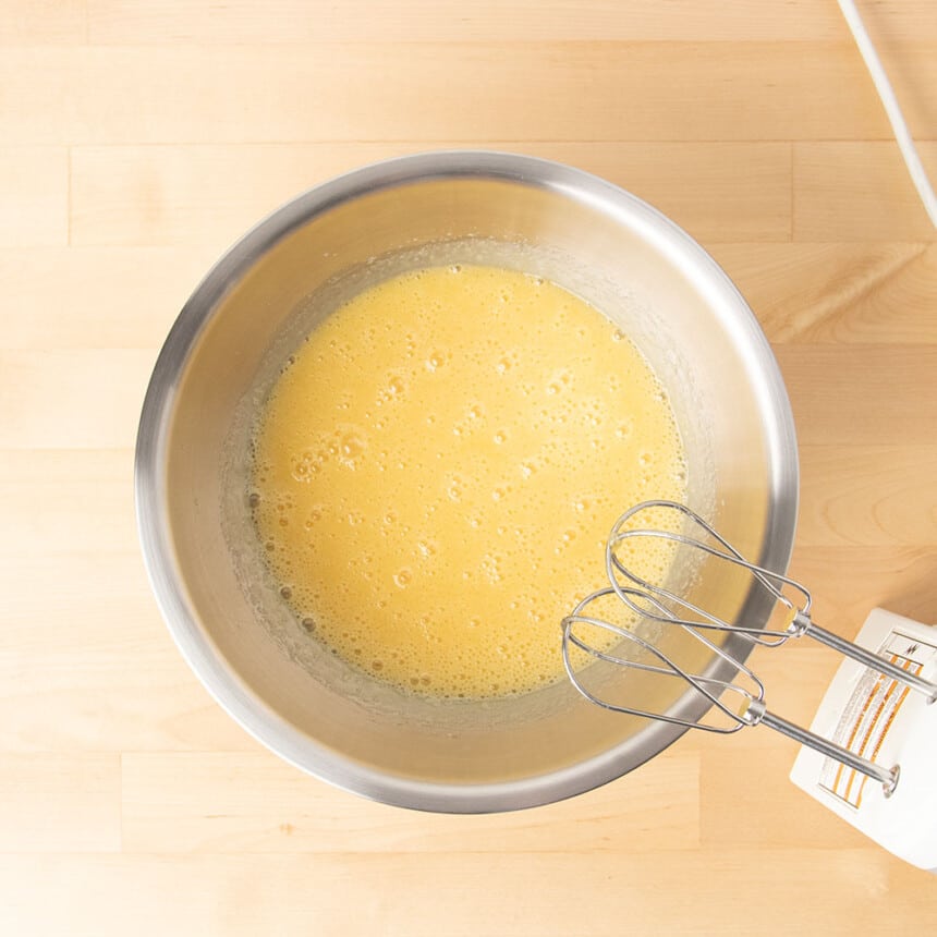 Metal mixing bowl with butter and sugar beaten with eggs into frothy yellow mixture