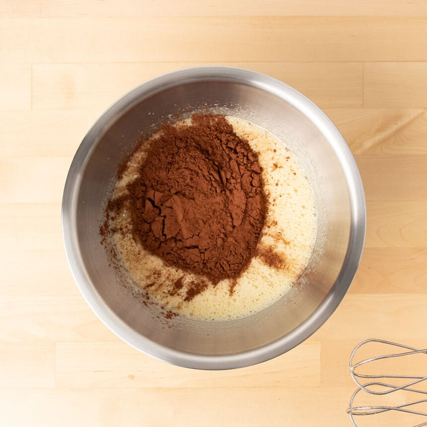 Dark brown cocoa powder on top of frothy yellow mixture in mixing bowl