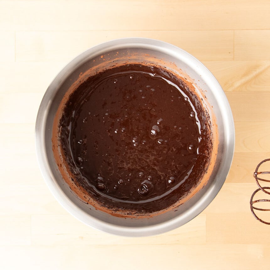 dark brown liquid in same metal mixing bowl with cocoa powder around rim of bowl