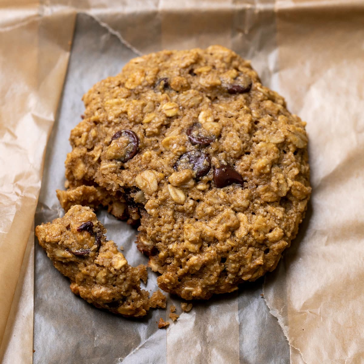 oatmeal breakfast cookie with raisins and corner broken on brown wax paper bag