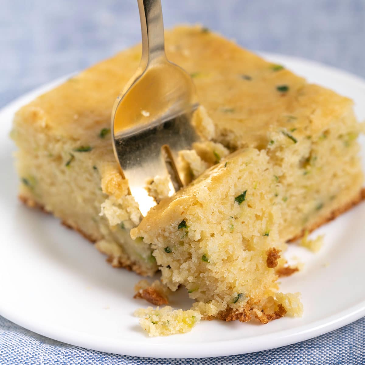 plain slice of gluten free zucchini cake with gold fork on small white plate