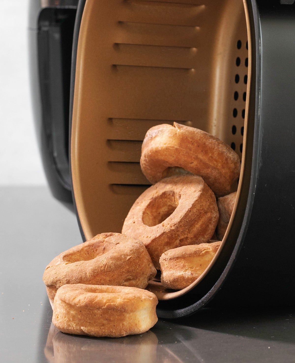 Brown baked donuts falling out of an air fryer basket turned on its side