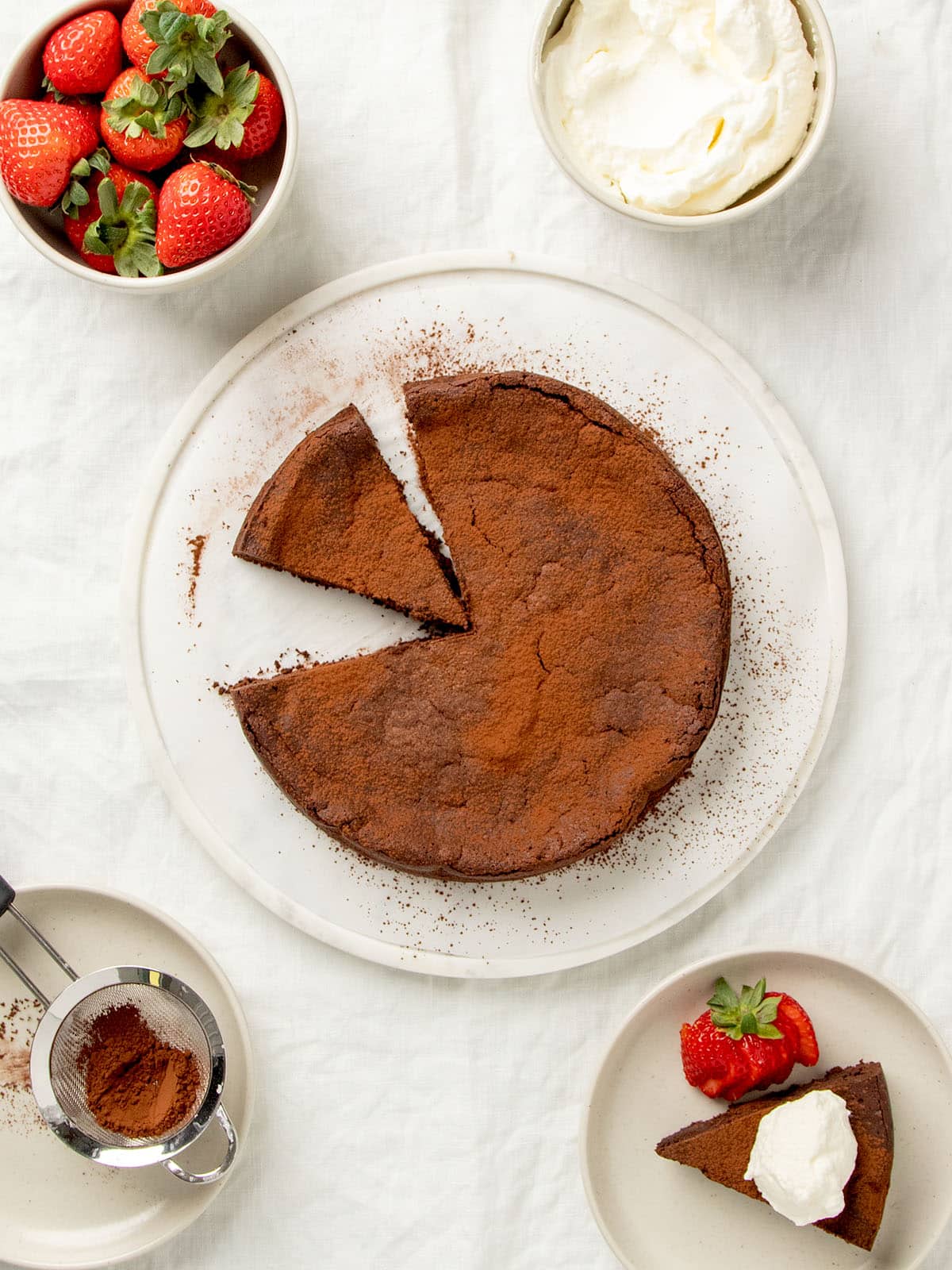 Overhead view of the chocolate cake with cocoa powder with one slice cut and one slice missing.