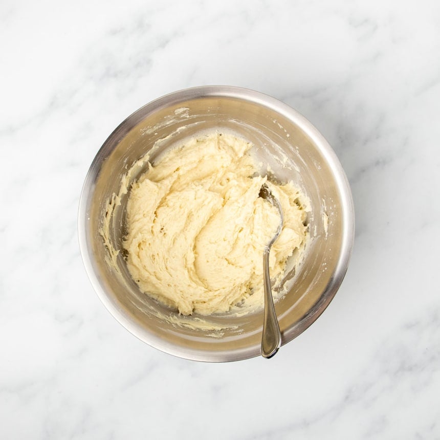 light yellow thick but shapeless bread dough in mixing bowl with large metal mixing spoon