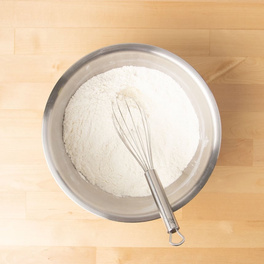 large round metal mixing bowl with dry ingredient and wire whisk