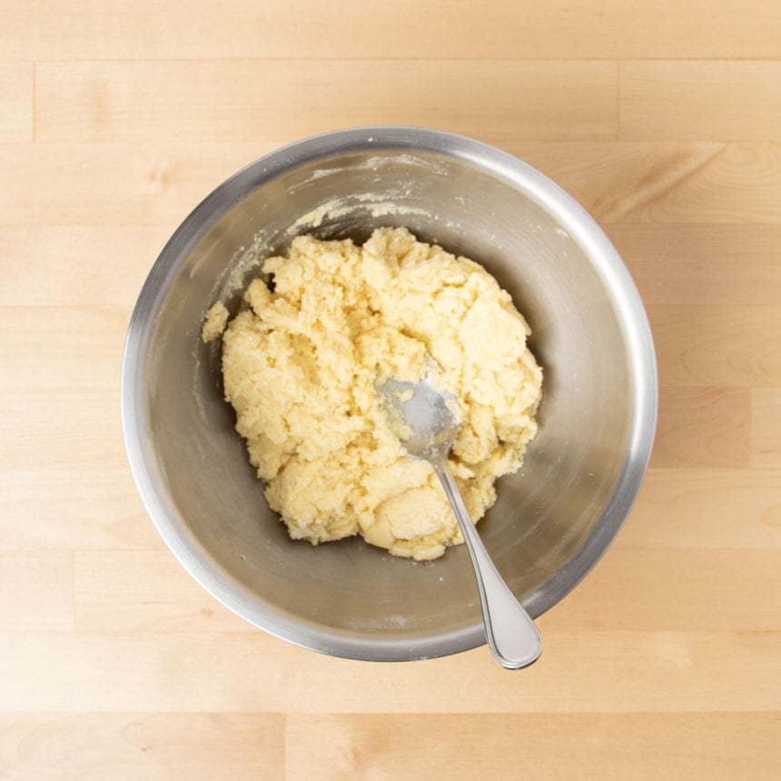 light yellow cookie dough with eggs mixed in with metal mixing spoon