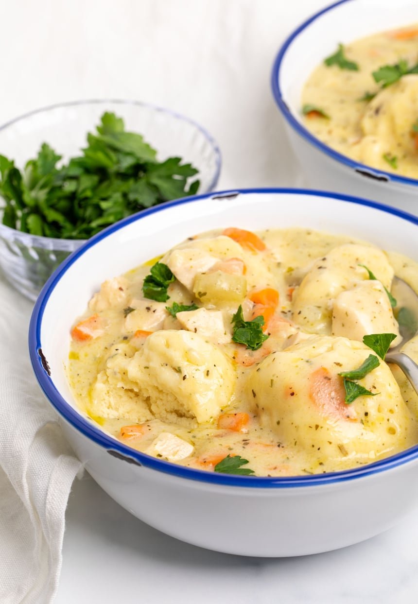 white bowl with 3 dumplings, one broken in half, with parsley leaves, white cloth, and metal soup spoon