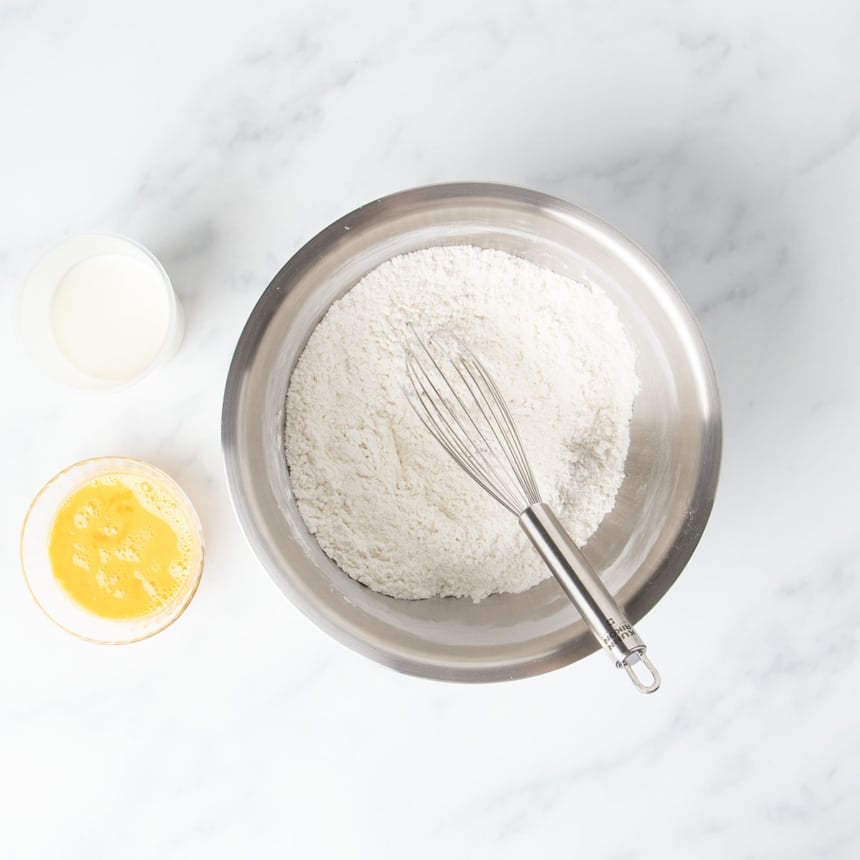 Round metal mixing bowl with white flour and wire whisk