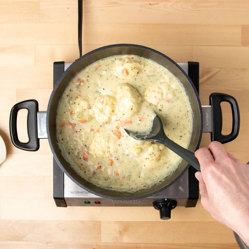 hand using black mixing spoon to mix raw dumplings into hot light tan soup