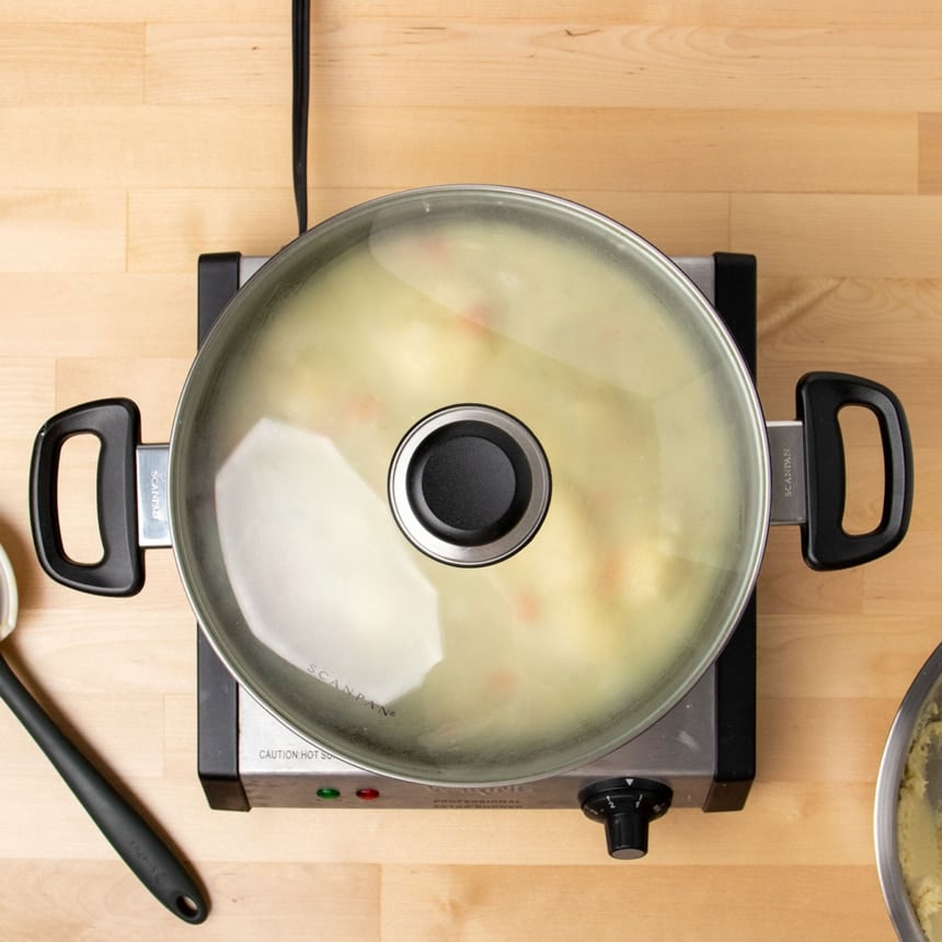 black pot with glass cover with simmering light tan soup inside