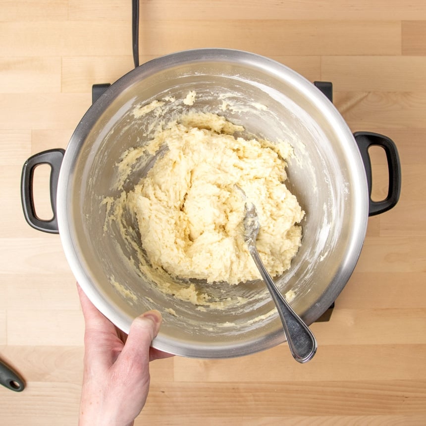 overhead image of raw light yellow dumpling batter in same mixing bowl with metal mixing spoon