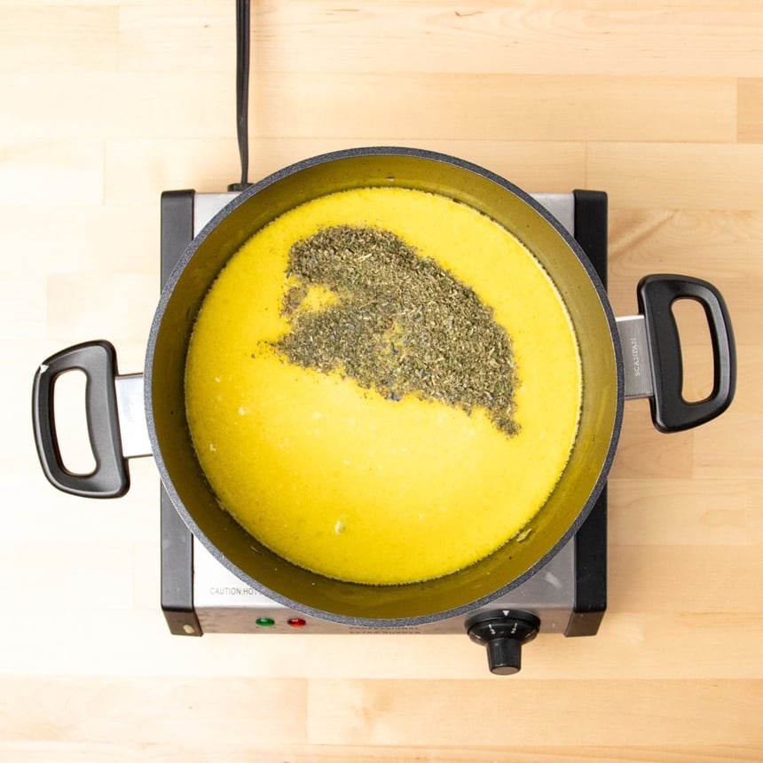 green and purple herbs de provence sitting on yellow liquid in black pot