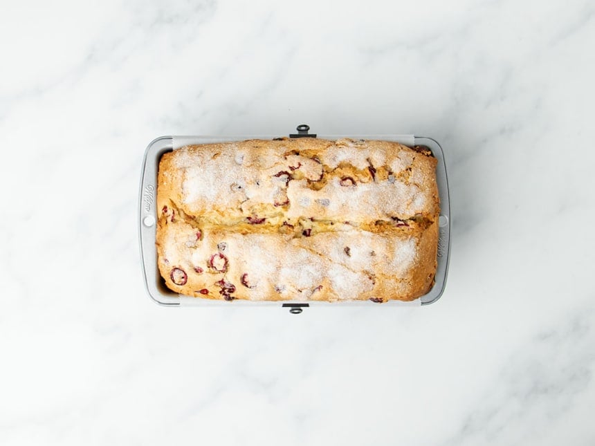 light brown baked gluten free cranberry bread with white sugar on top in metal loaf pan