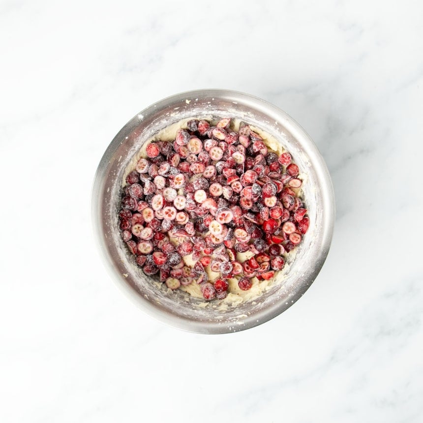 Halved fresh cranberries on top of light yellow batter in bowl