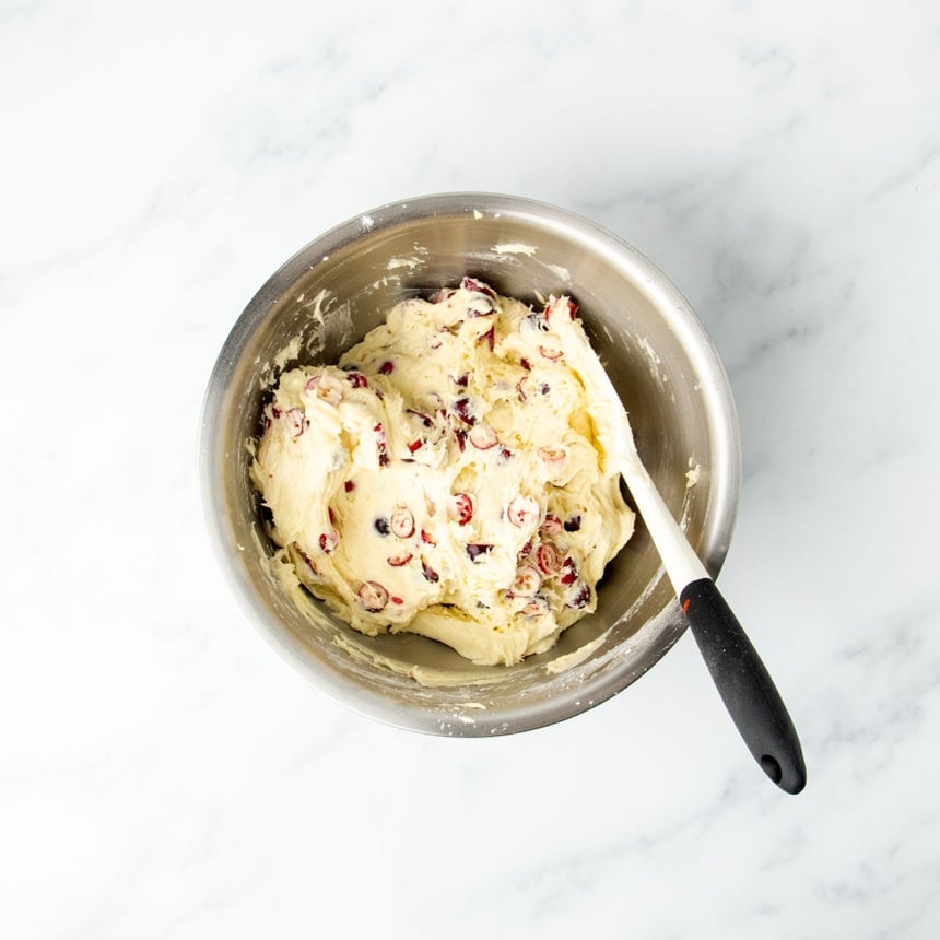 Raw cranberry bread batter with cranberries mixed in with white spatula with black handle in bowl