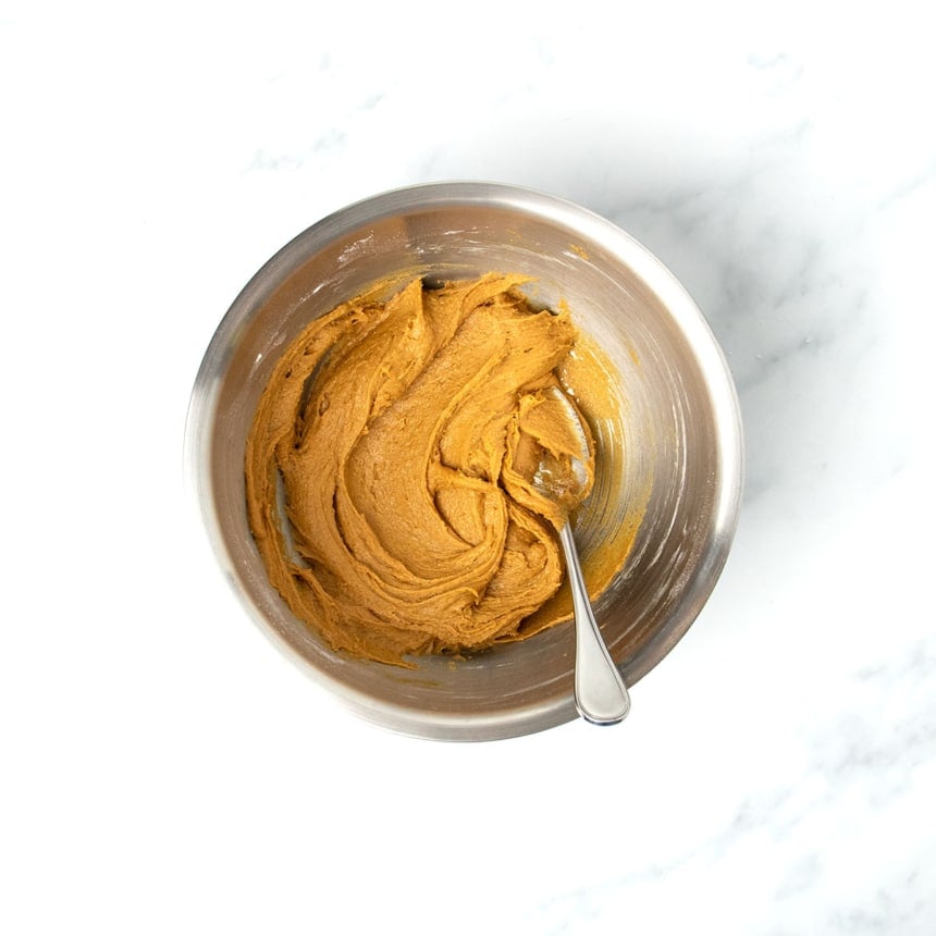 same bowl with soft light brown mixed gluten free molasses cookie dough with metal mixing spoon