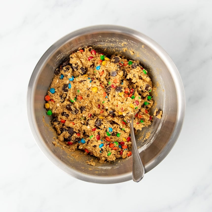 Raw thick light brown gluten free monster cookie dough with colored candy pieces and chocolate chips in same mixing bowl