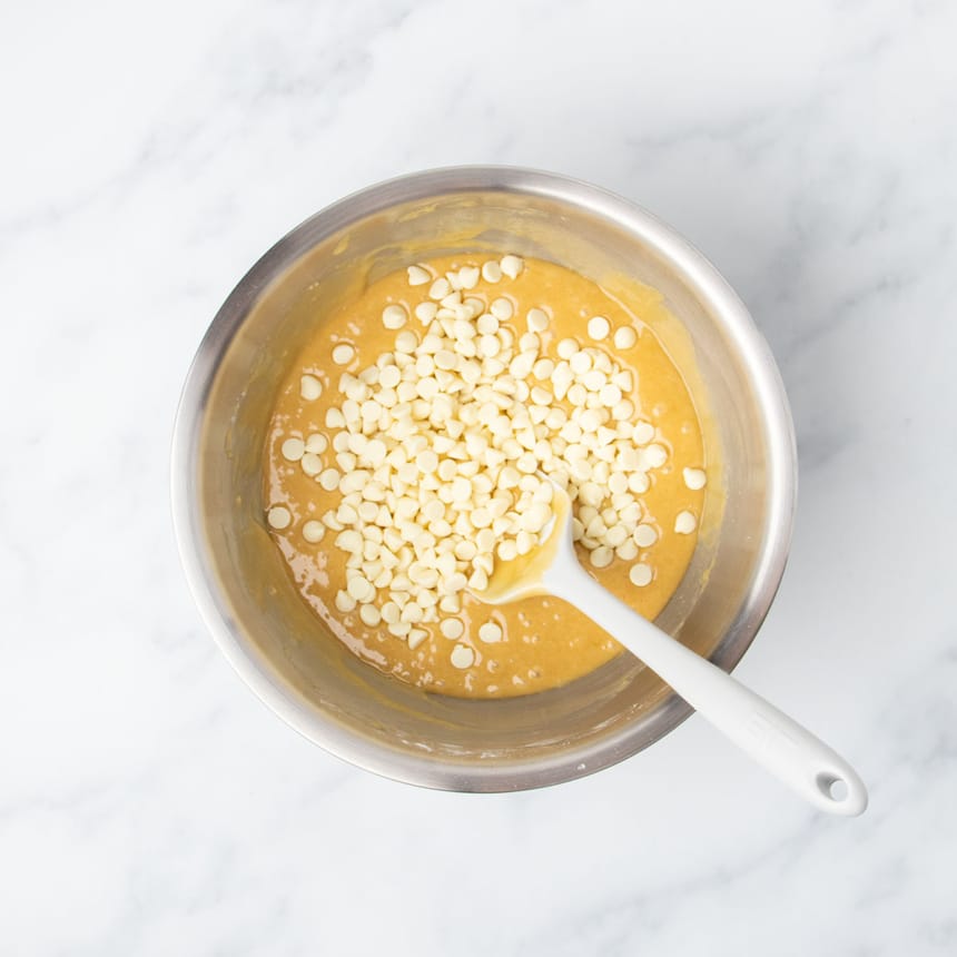 white chips on top of light brown mixture in mixing bowl with white spatula