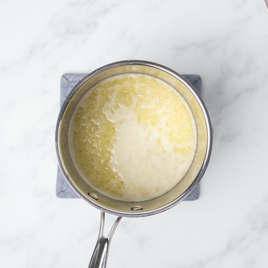 Round metal saucepan with simmering melted butter and sugar mixture on blue potholder