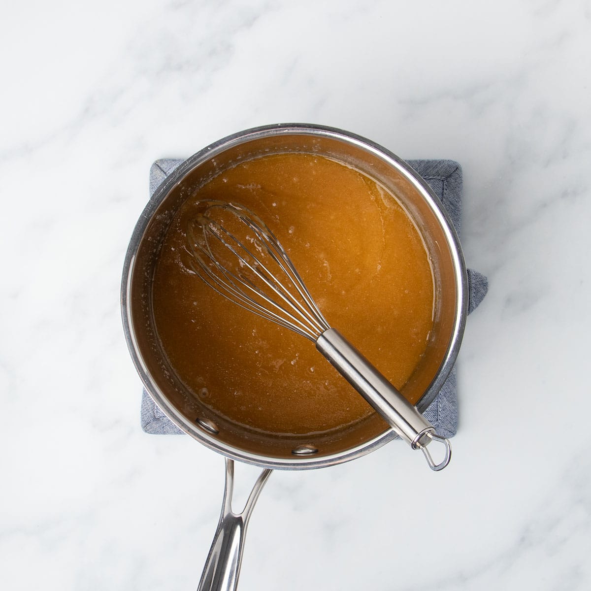 Saucepan with wire whisk and whisked dark brown liquid mixture