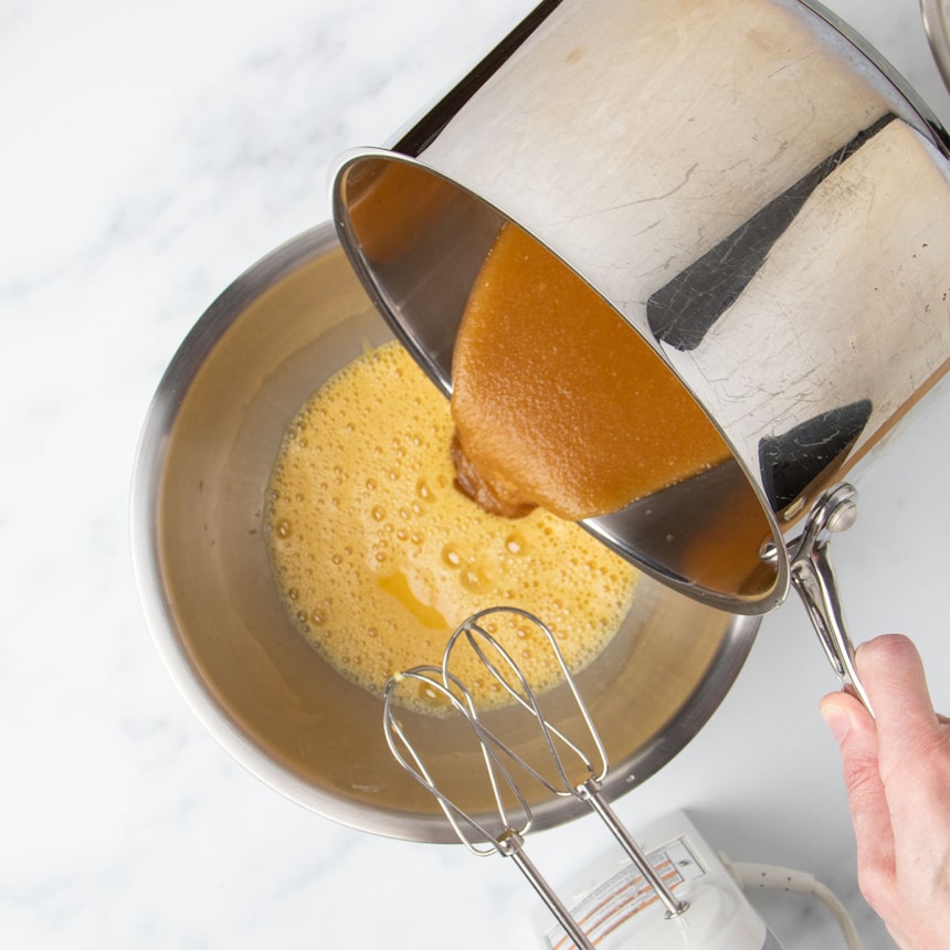 Hand tipping saucepan with brown liquid into mixing bowl with beaten eggs