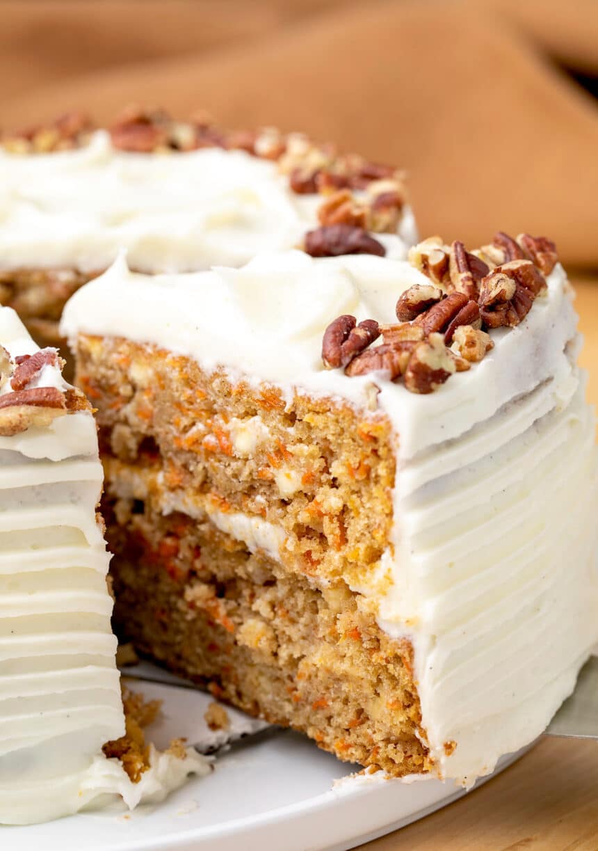 Closeup of slice of carrot layer cake being taken from whole cake on platter